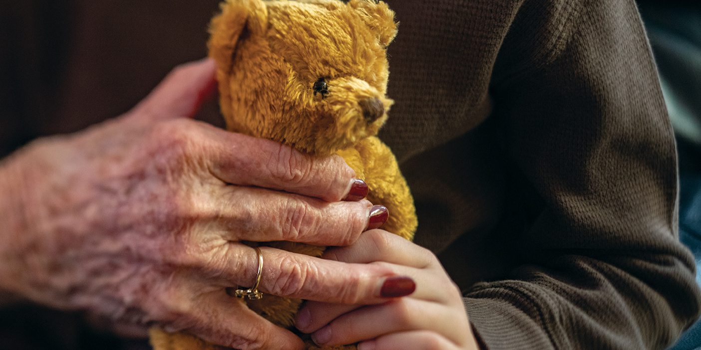 Hands, one young, one old, grasp a golden-brown teddy bear.