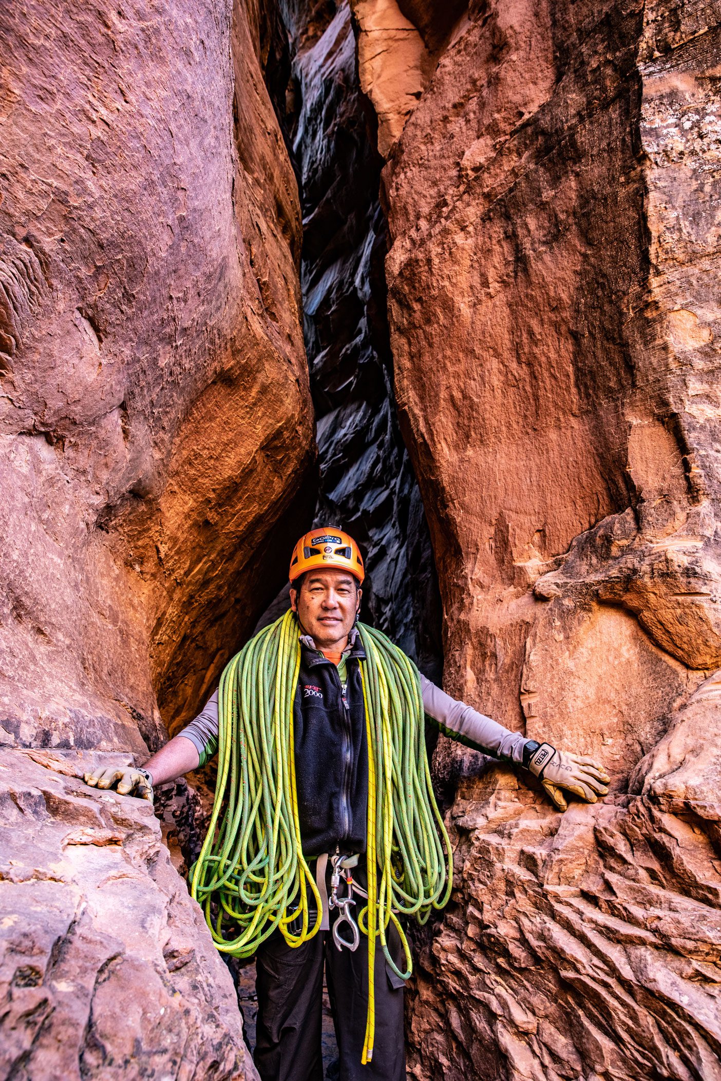 Stacy Taniguchi emerges from a slot canyon with hundreds of feet of climbing rope draped around his shoulders.