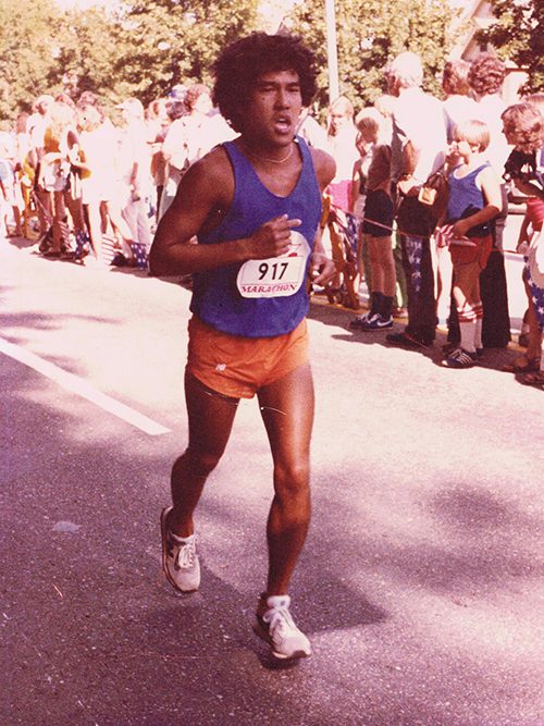 A photo of Stacy Taniguchi running in a marathon. His hair is styled in a perm, reflecting the style of the day.