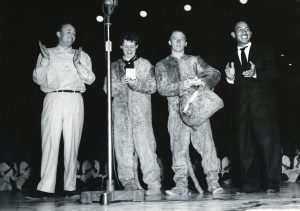 Four people, two of them in Cosmo costume, stand on the playing floor of the Smith Fieldhouse in 1956.
