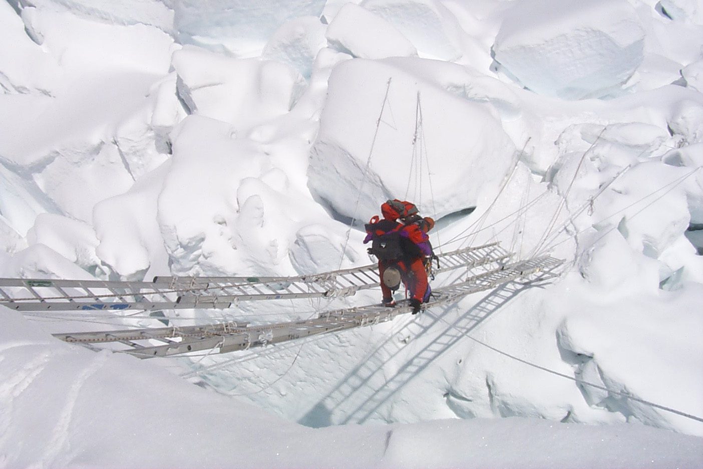 A climber crosses a ladder set across a giant crevasse on Everest.