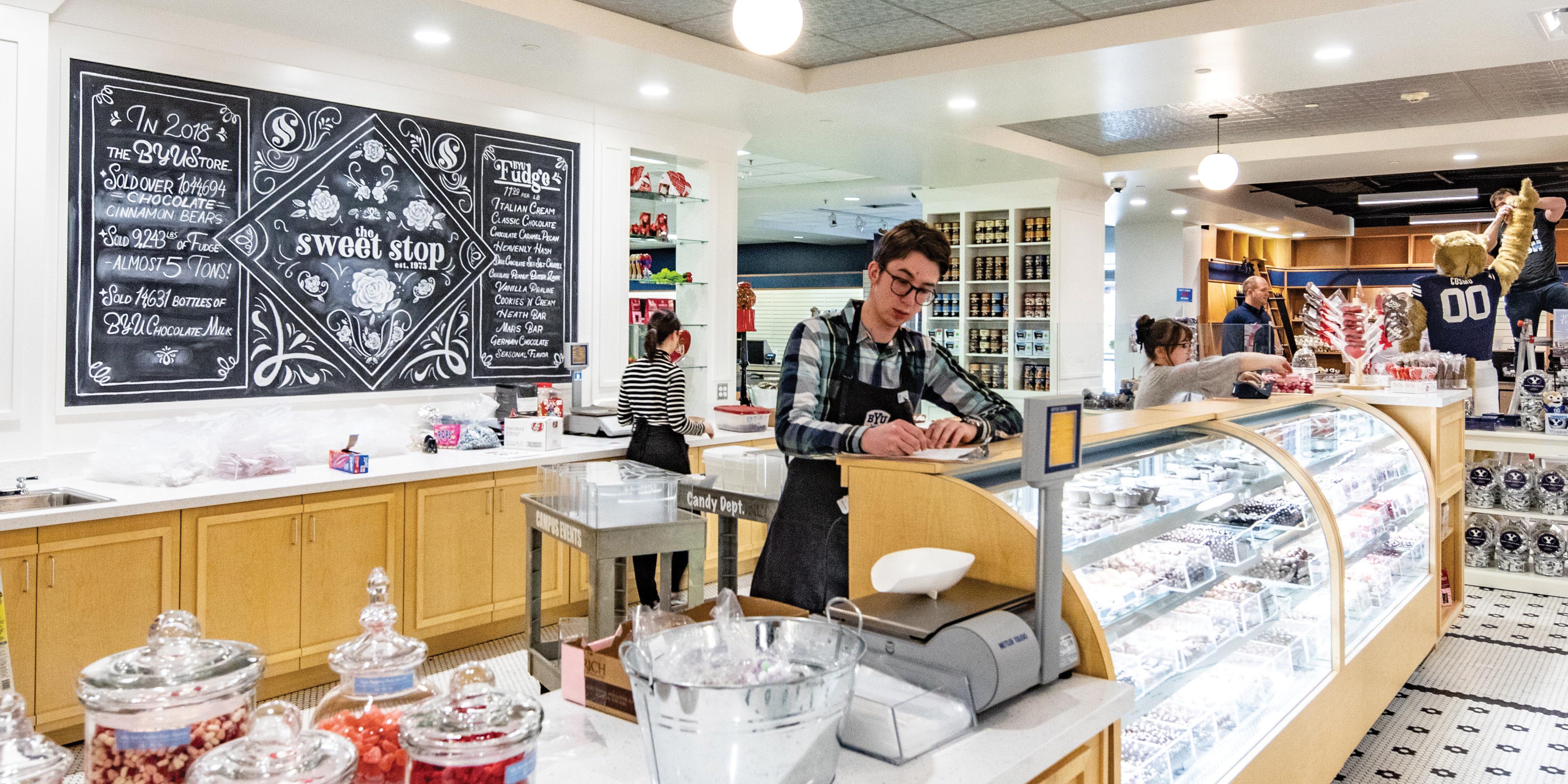 An image of the main glass counter of the Sweet Stop. A young man stands at the cashier and brightly colored jars are visible in the background