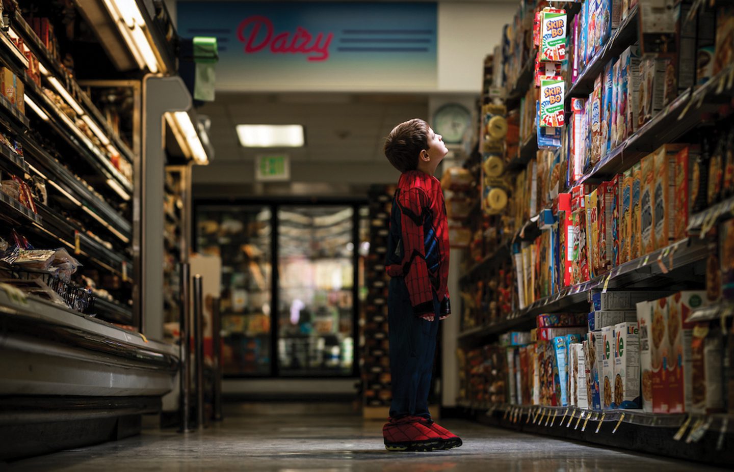 Child in Spiderman costume at the grocery store looking at products in an aisle.