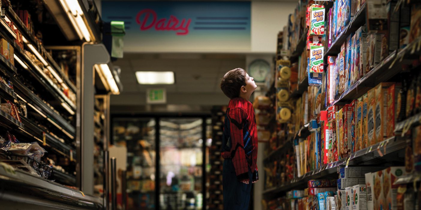 Child in Spiderman costume at the grocery store looking at products in an aisle.