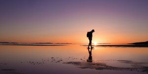 silhouette of man walking through water at sunset