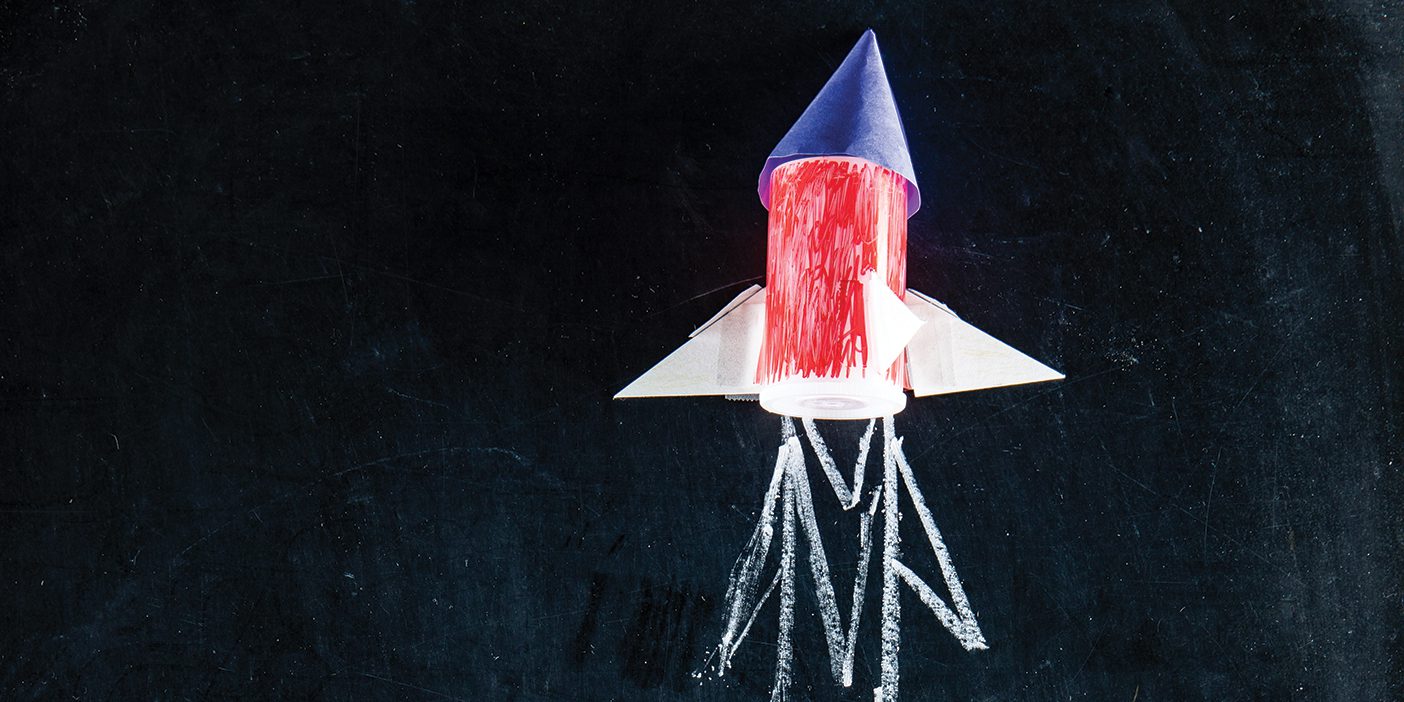 A paper rocket blasts off on a chalkboard with chalk exhaust drawn below it