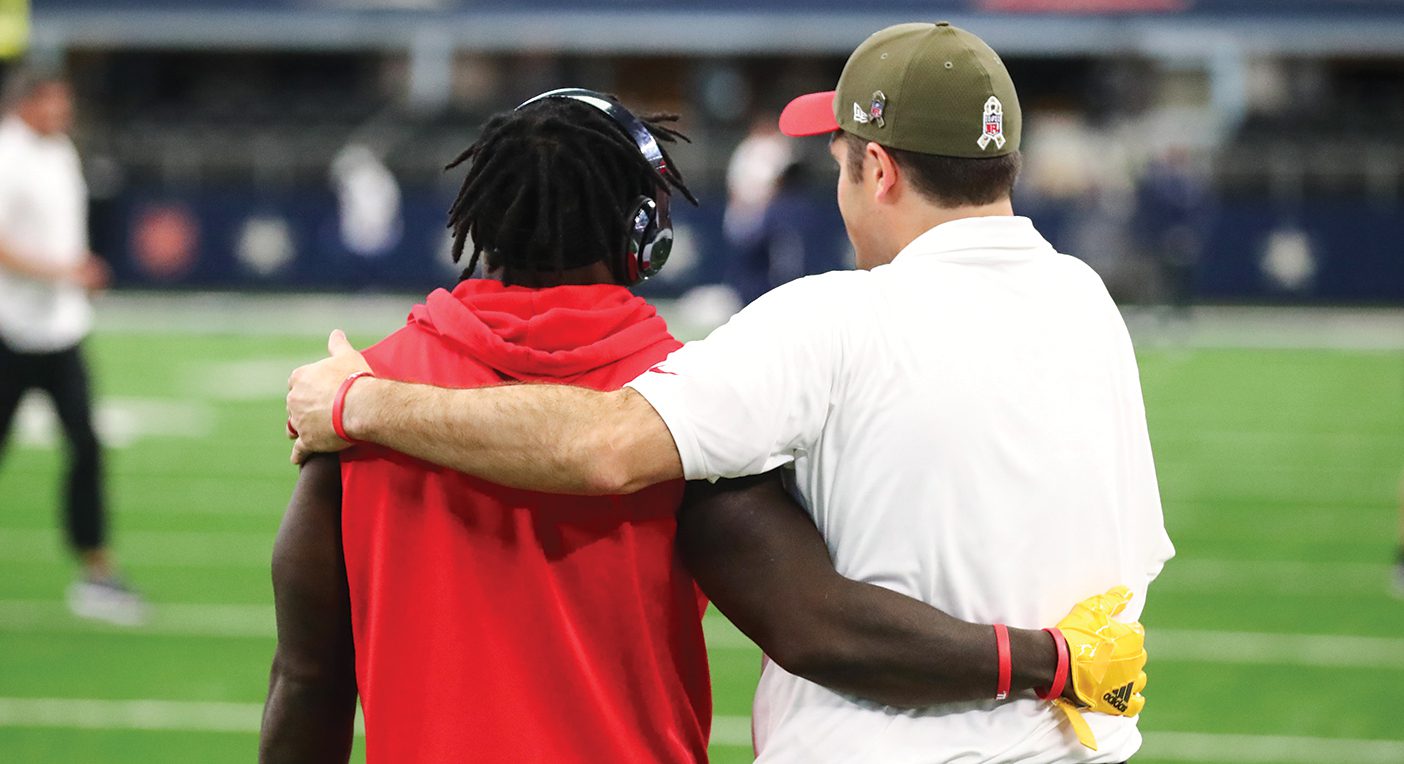 A Kansas City Chief's player and Porter Ellett stand with arms around each other's backs, with their backs facing the camera.