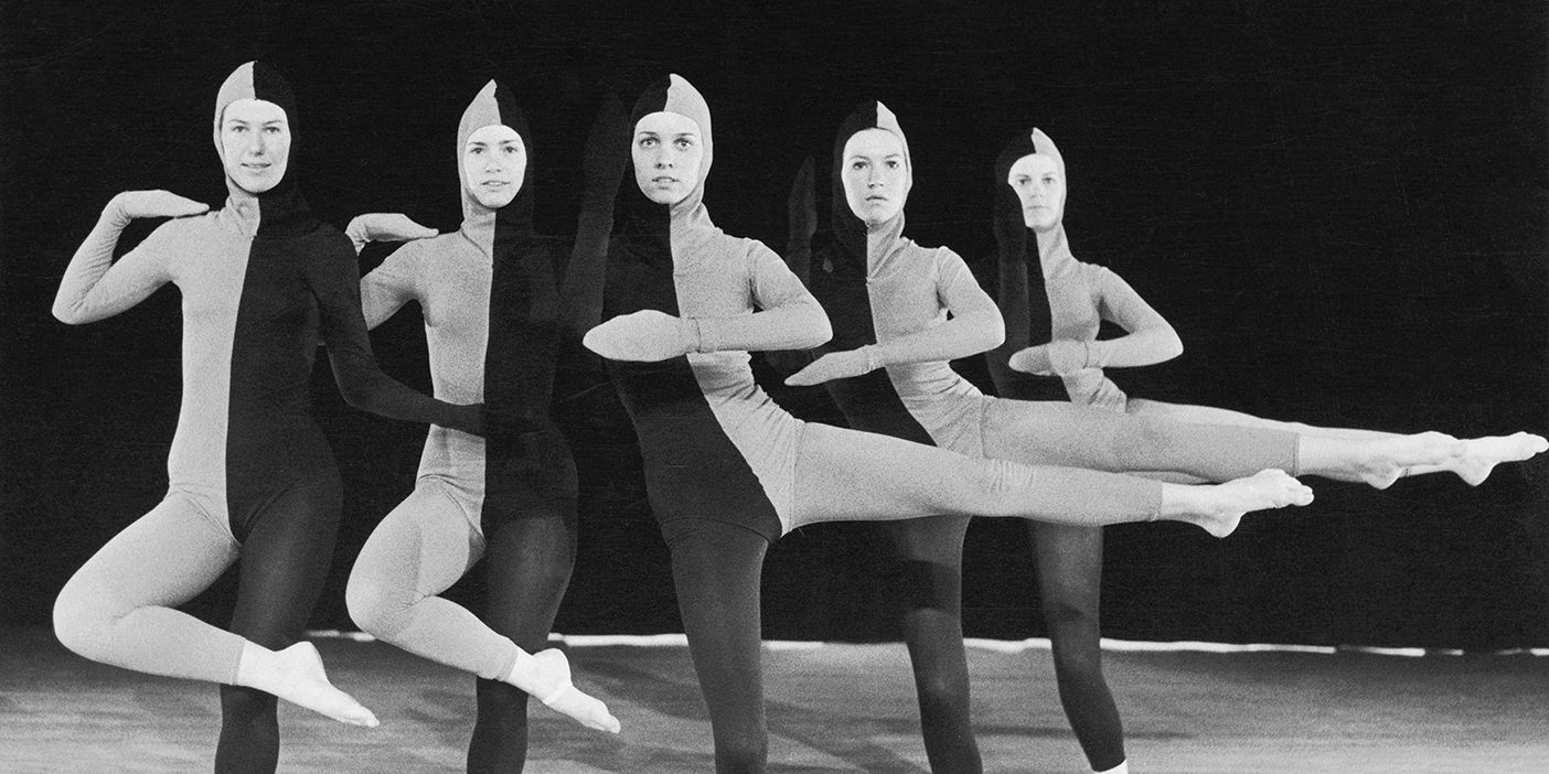 Five dancers dressed in full body tight suits split in half with gray and black take dancing poses for the camera.