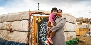 A Mongolian woman holds her daughter outside of their retrofitted ger, or traditional home.