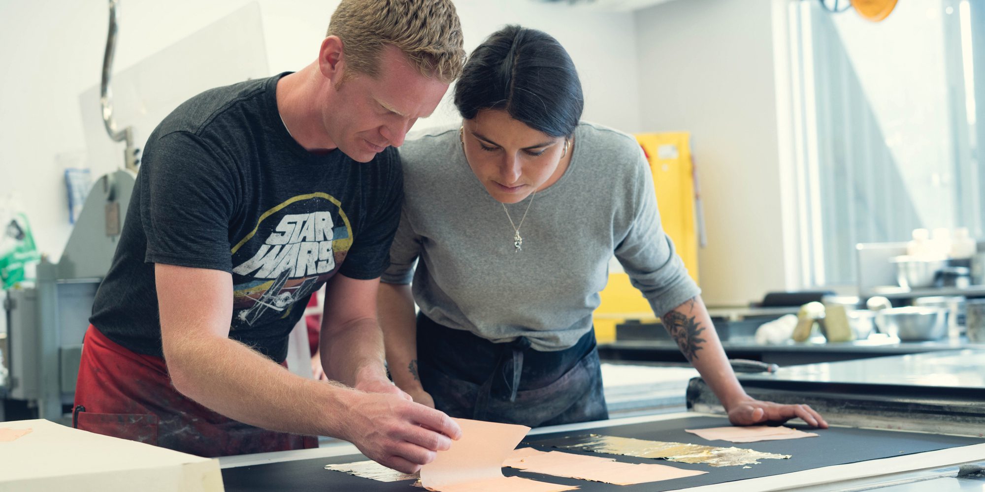 Brandon Gunn and a woman work on prints in a studio.
