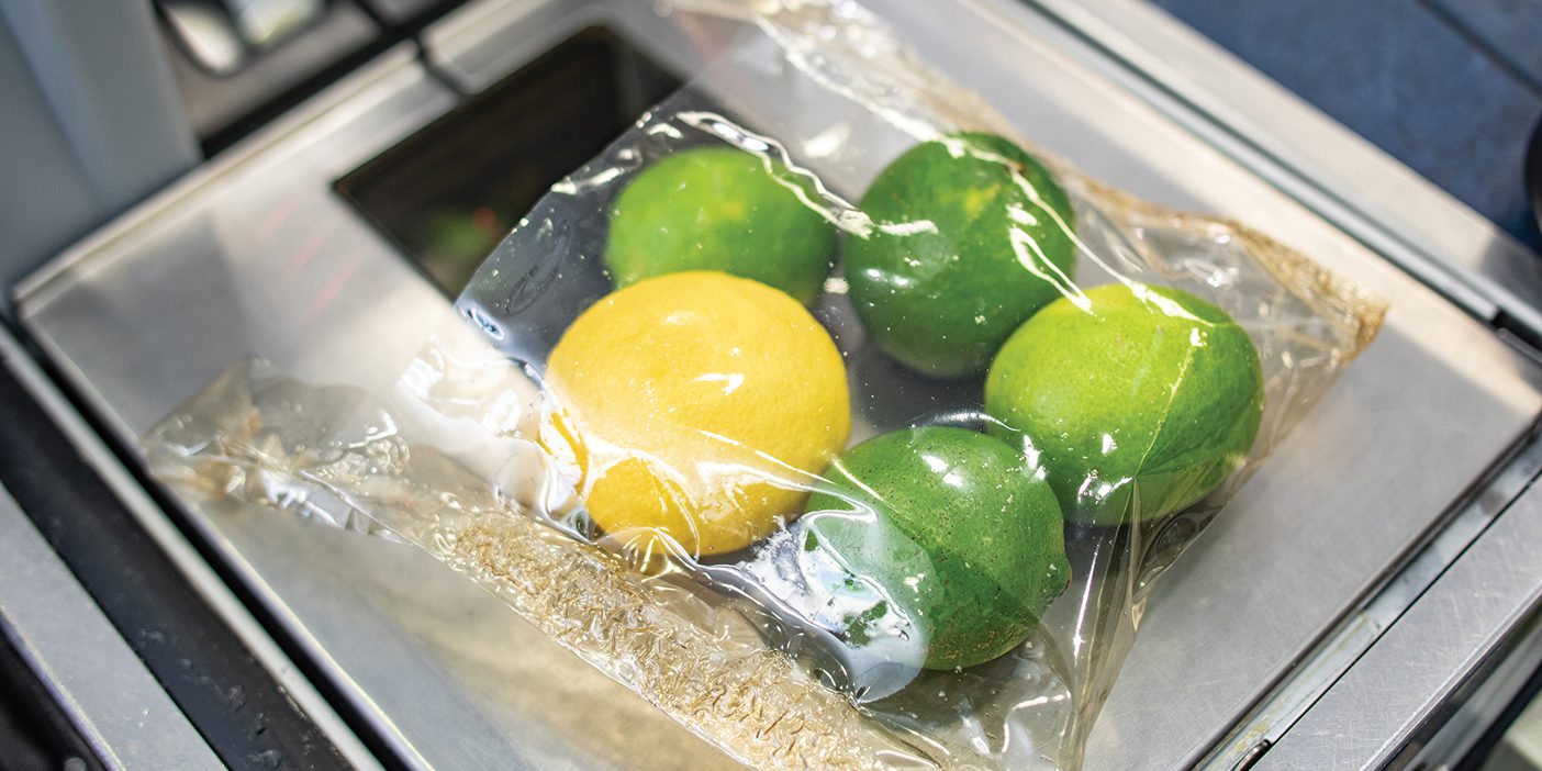 A biodegradable bag holds a lemon and four limes on top of a grocery store scanner.