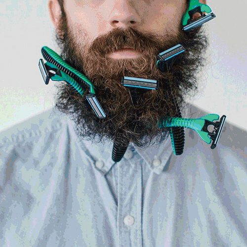 A portrait of a bearded man from the nose down with razors stuck in his beard.