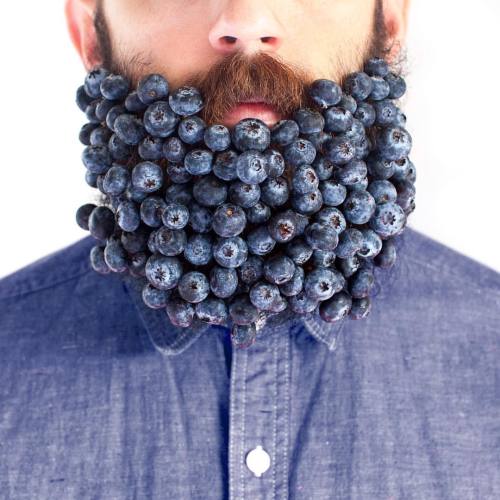 A portrait of a bearded man from the nose down with blueberries stuck in his beard.