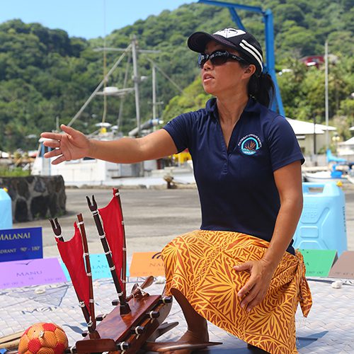 Furuto kneels above a wooden model of a canoe teaching and directing their voyage.