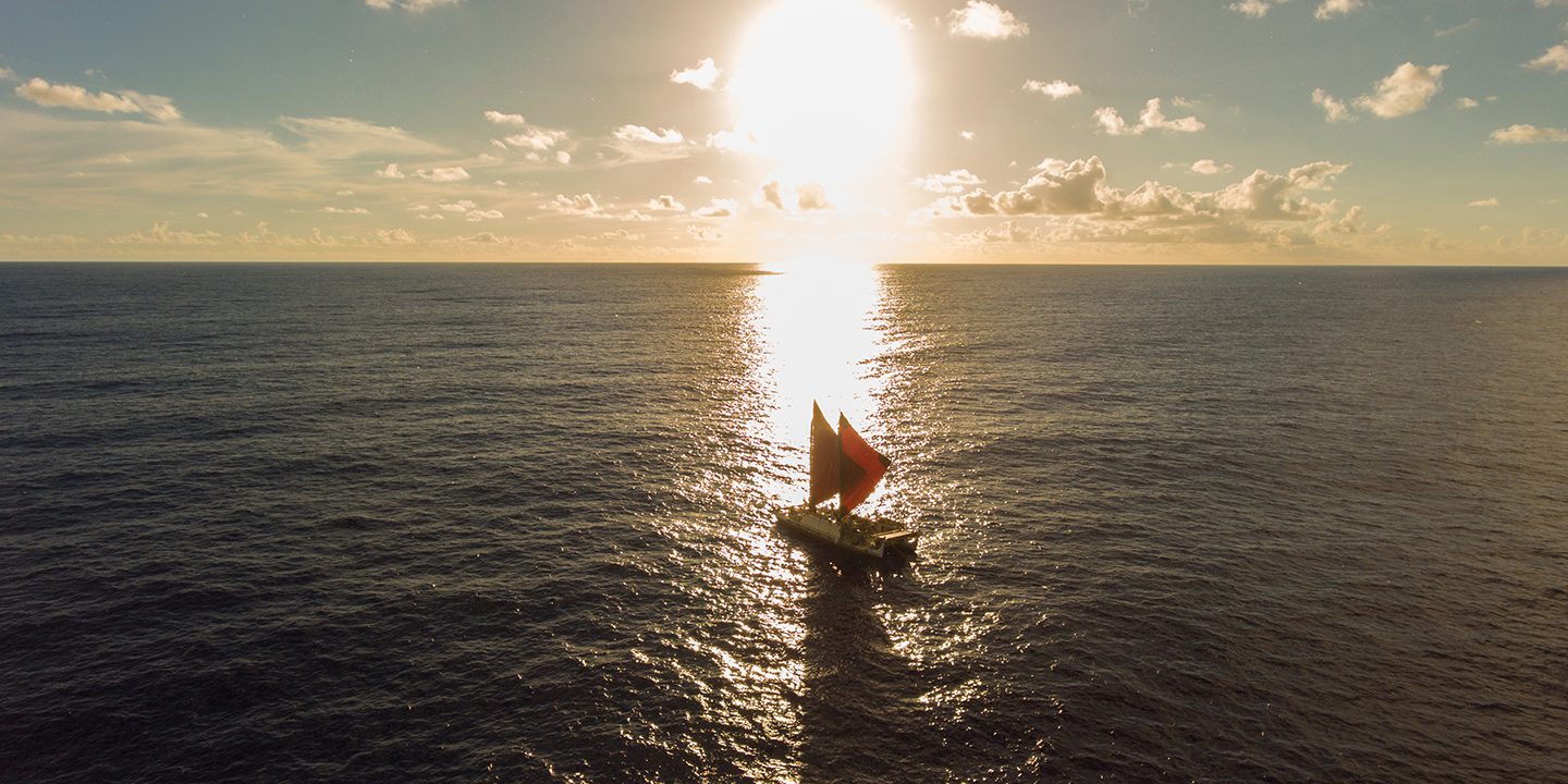 An ocean sailing canoe on the ocean sailing into the sun