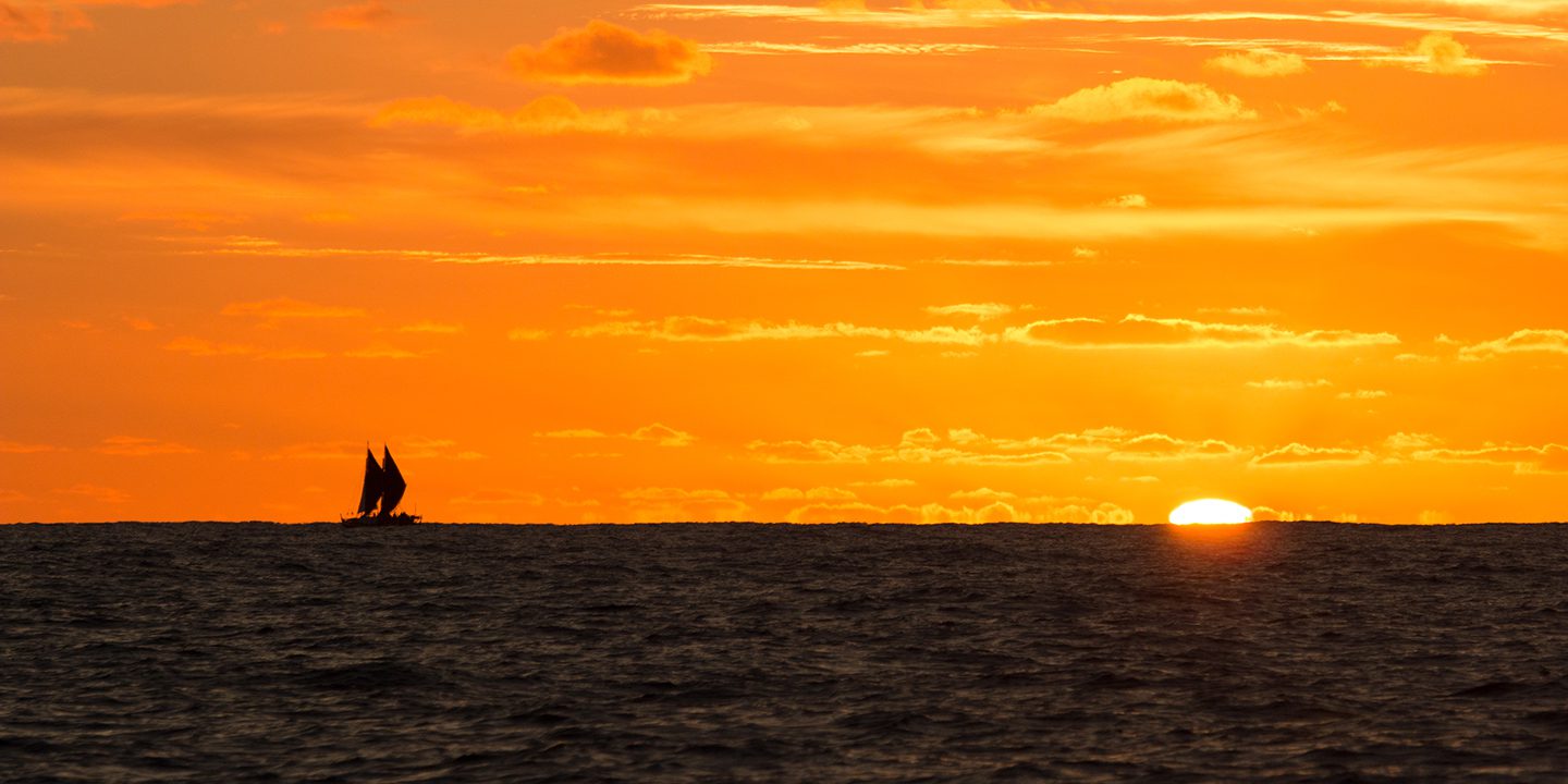 Canoe sails into the sunset on the ocean
