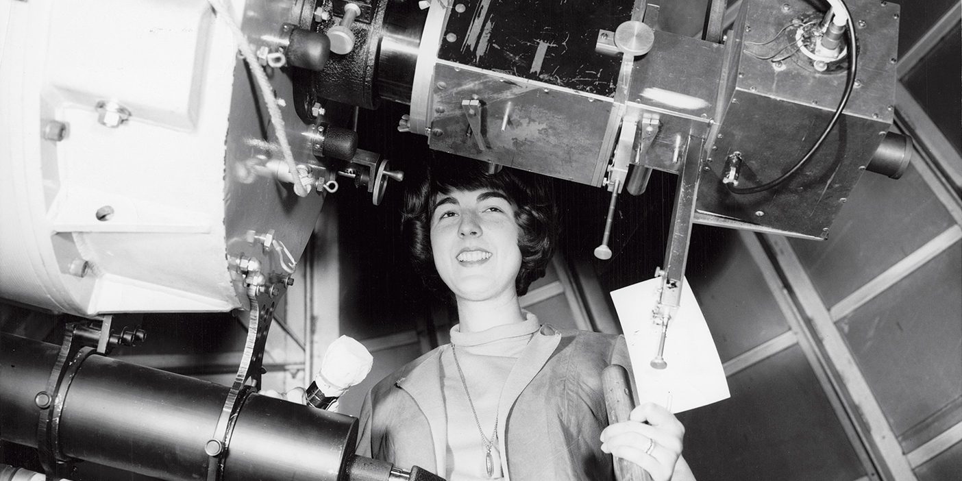 BYU student Helen Sievers smiles behind a large telescope in this archival photo.