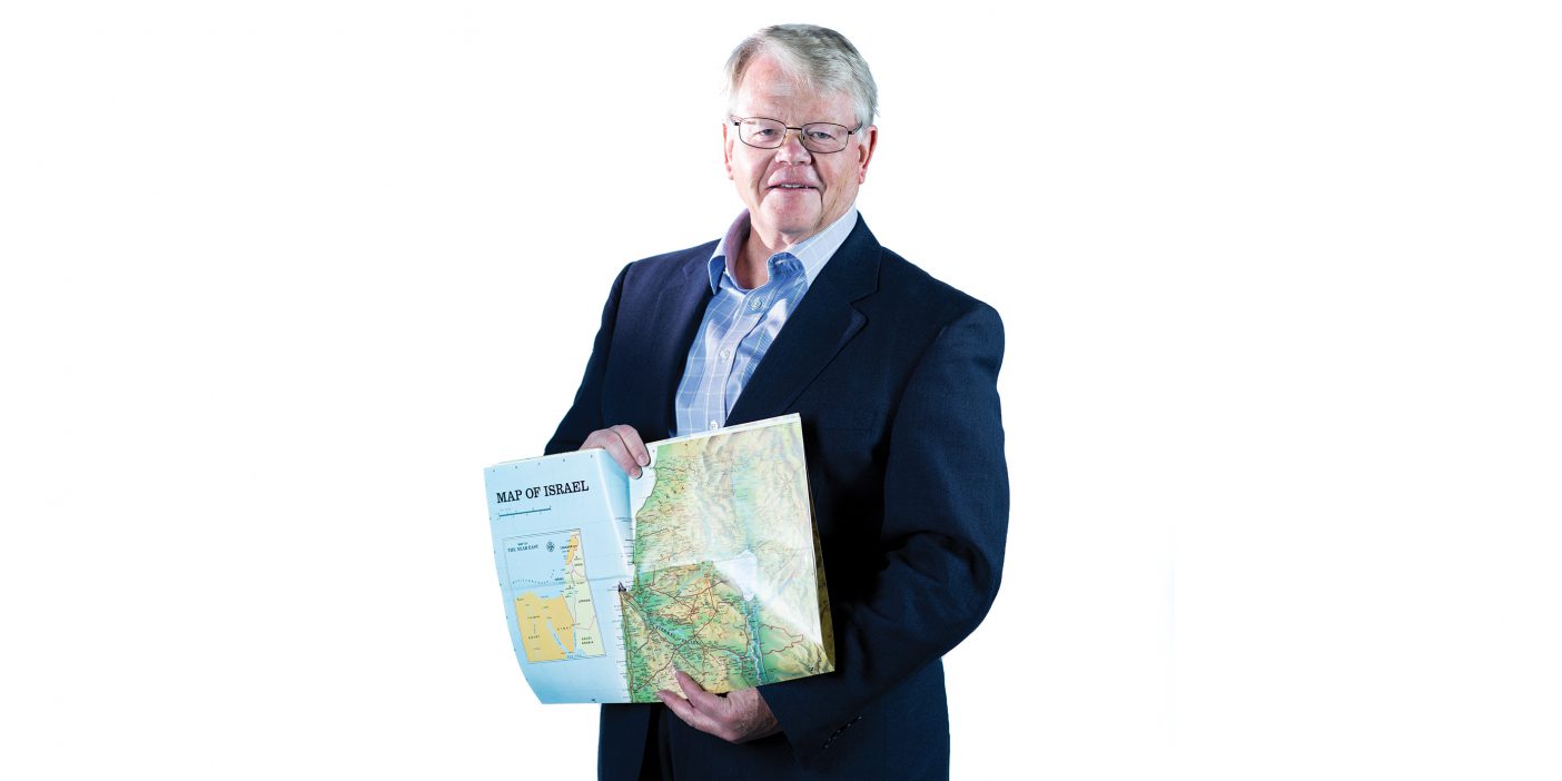 Andrew Skinner, wearing a dark suit coat, holds a map of Jerusalem.