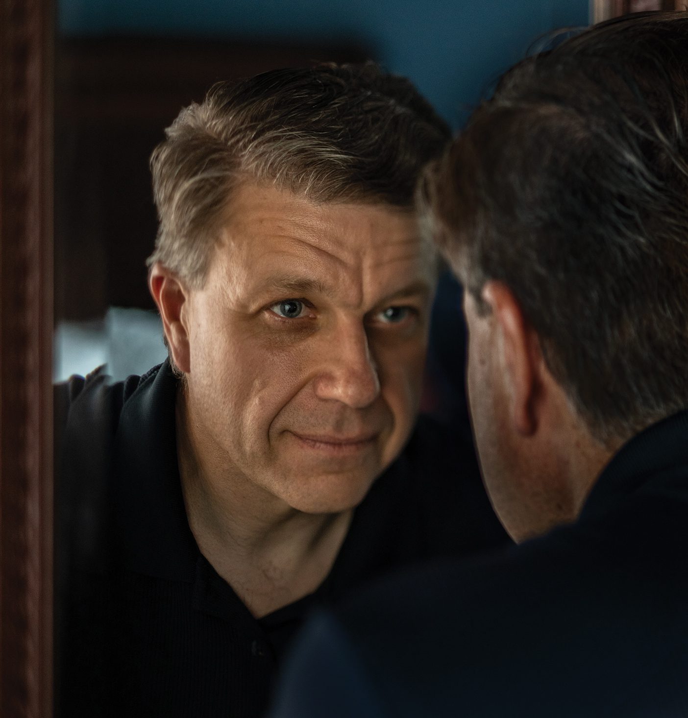 A handsome middle-aged man practices self-compassion by looking at his reflection in a mirror and imagining he is a person who cares deeply about himself and others.
