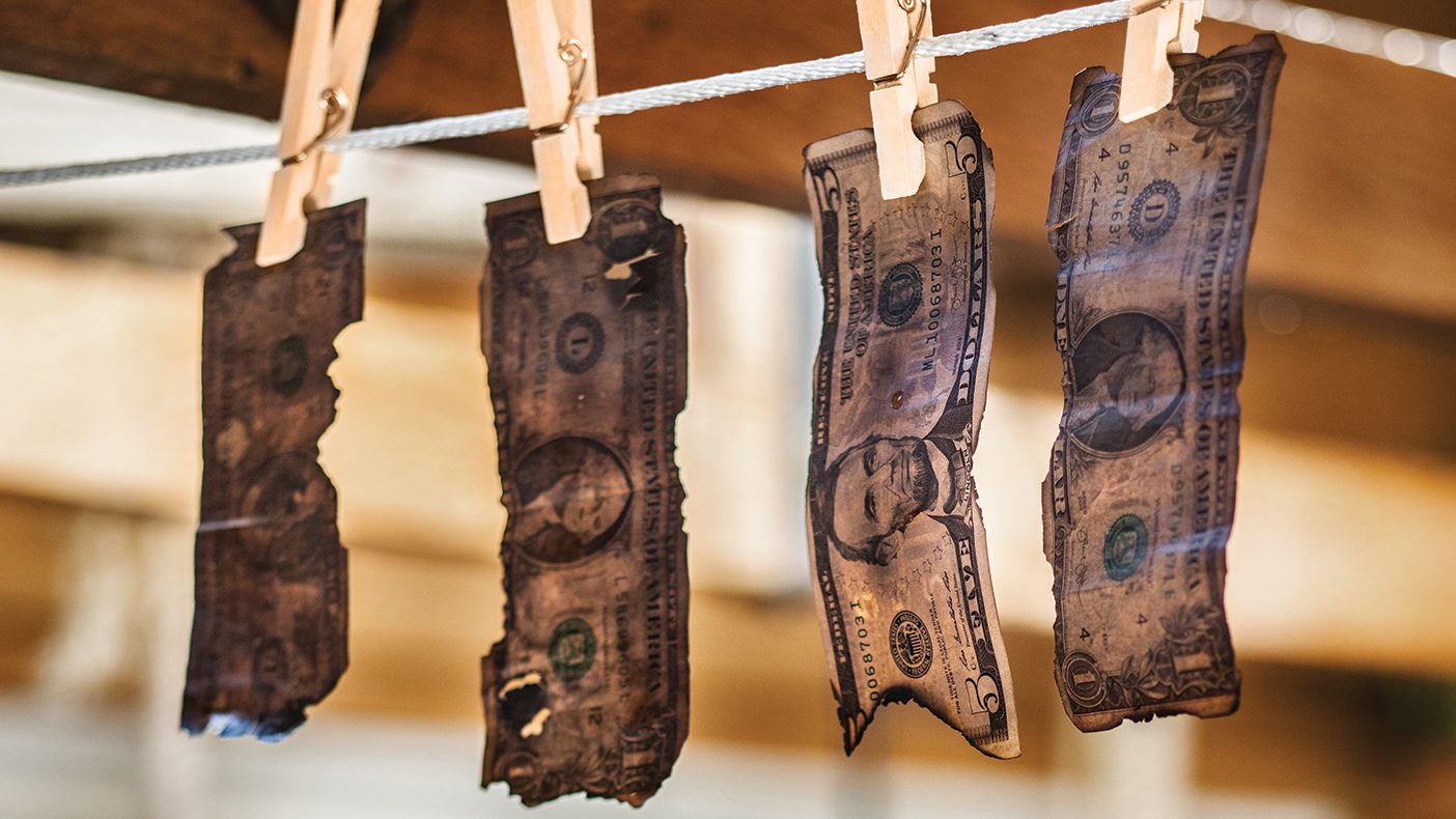 Fire-blackened money is attached to a line with clothespins.