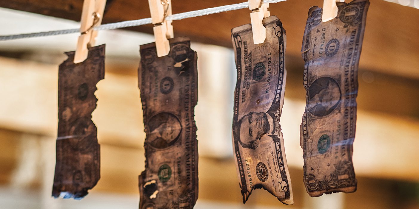 Fire-blackened money is attached to a line with clothespins.