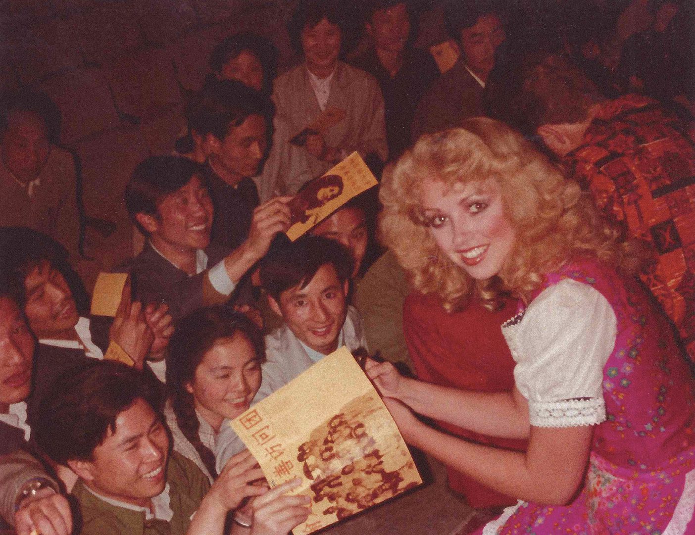 Jenny Fisher smiles at a camera while signing autographs from audience members in China.