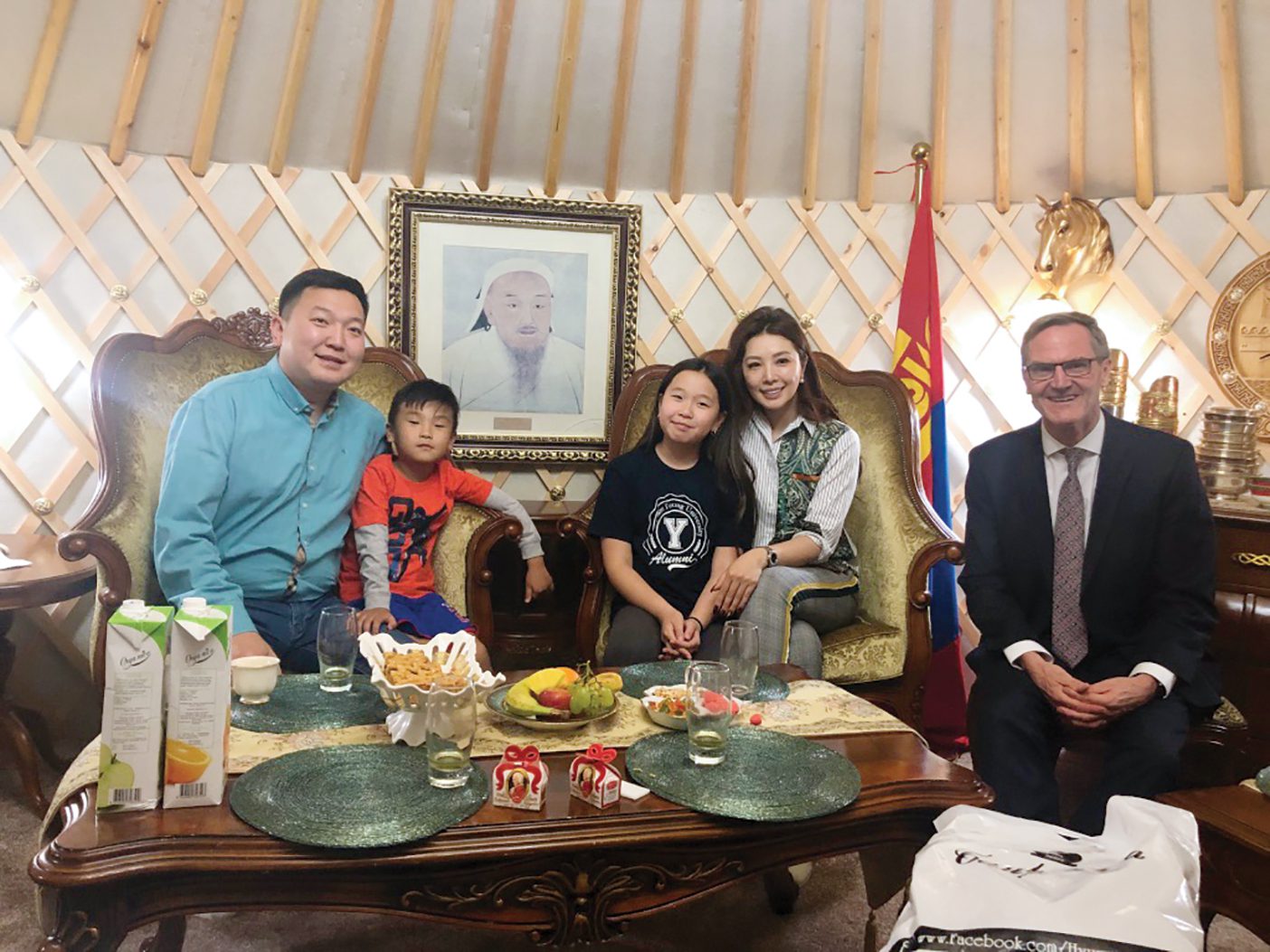 A man sits with a Mongolian family of one father, one mother, one son, and one daughter inside a traditional Mongolian yurt home.