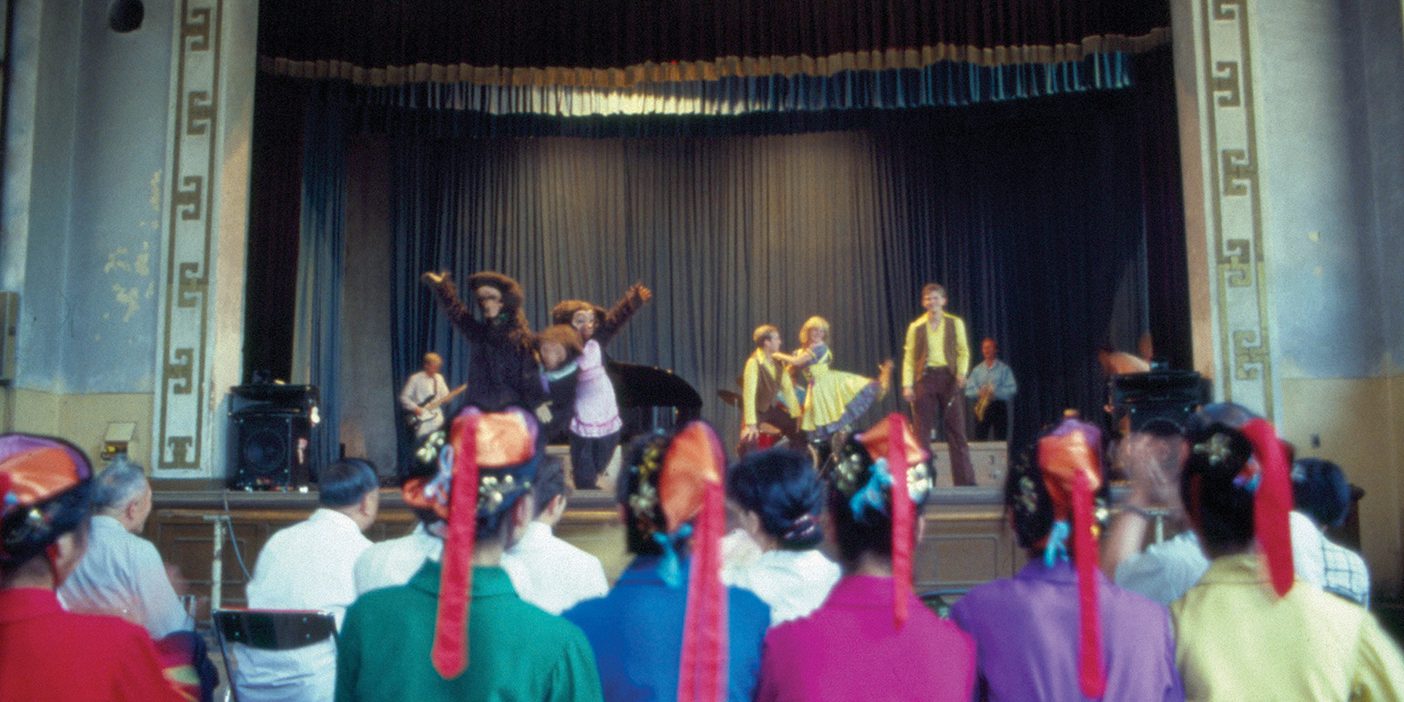 A group of BYU performers entertain onstage in China. An audience, including Chinese performers in traditional dress, are in the foreground.