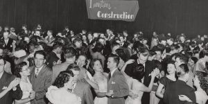 A crowd of students in a 1950s-era picture dance in an assembly hall. The words