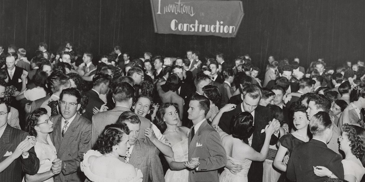 A crowd of students in a 1950s-era picture dance in an assembly hall. The words "Innovations in Construction" hang above their heads in the background.