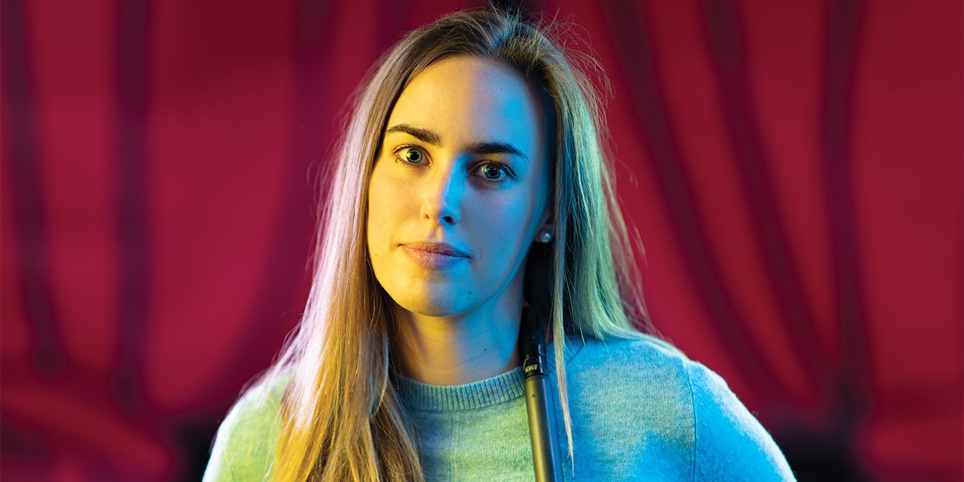 The 2019 BYU George H. Brimhall Memorial Essay Contest winner Hope Thomas stands in front of a red velvet curtain with a microphone draped around her shoulders. She tried stand-up comedy in her "semester-of-putting-myself-out-there."