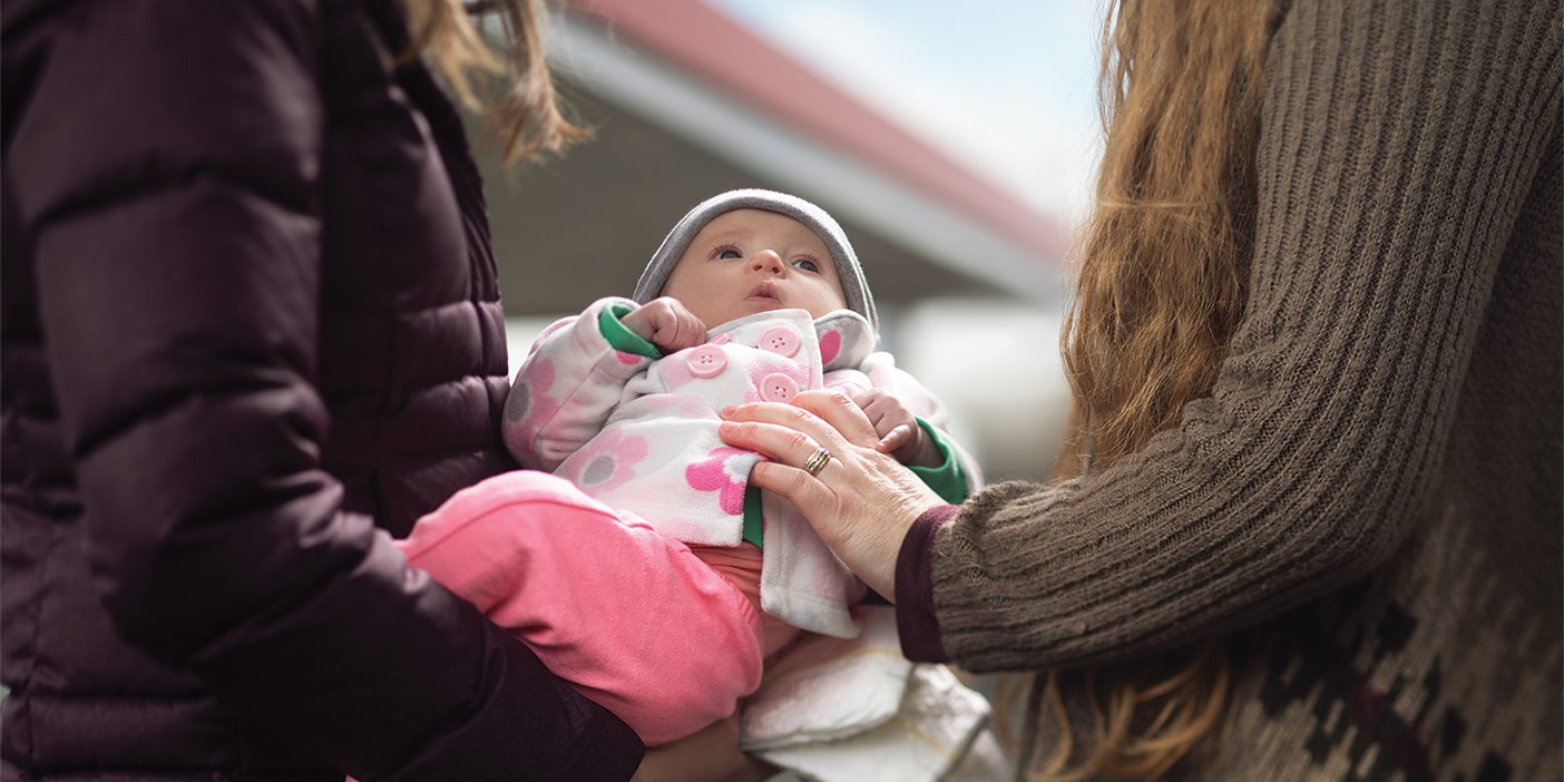 Two women—a caseworker and a foster mom—hold a baby girl and a handful of diapers in a gas station parking lot.