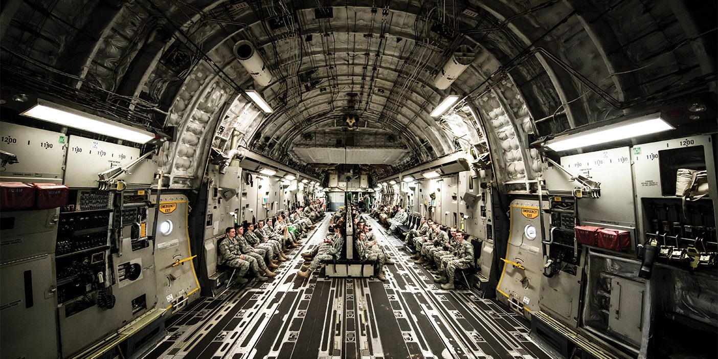 A group of ROTC members sit along the walls of a C-17 military plane.
