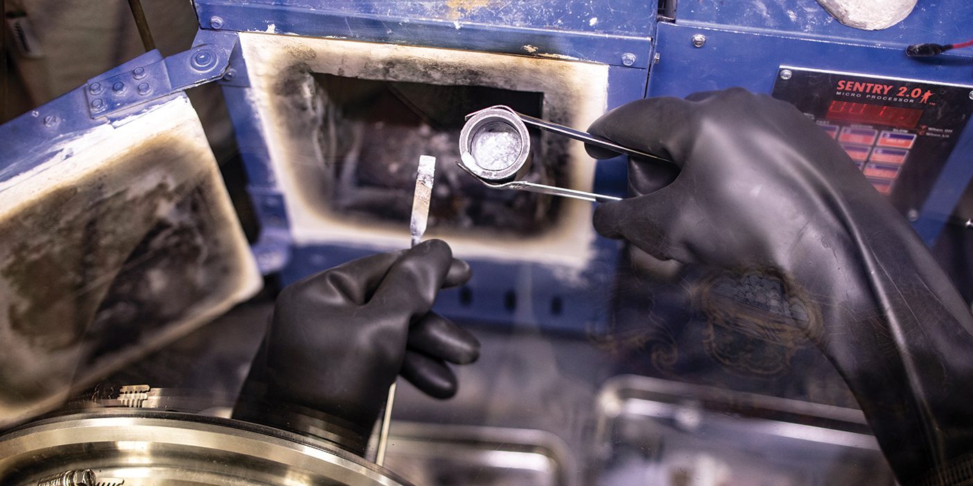 An image of Matthew Memmott's molten salt reactor lab, where Memmott is developing a new, cleaner nuclear energy process. Two gloved hands handle a small vial of molten salt.