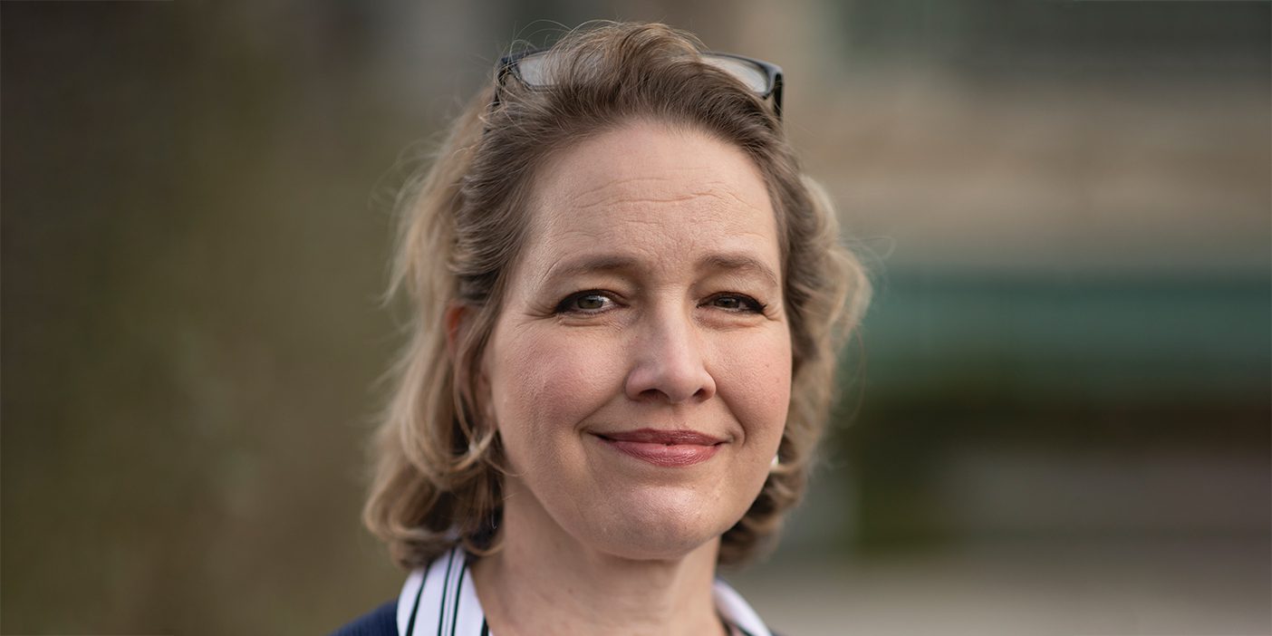 A smiling Deborah O. Himes wearing a lined button-shirt and blue cardigan, with reading glasses atop her head.