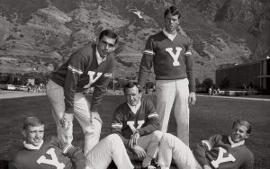 Five young male cheerleaders from 1968 wear plaid pants and sweaters with a big