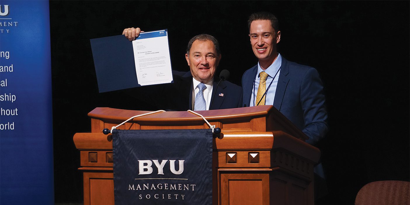 Gary Herbert stands at a podium, holding up a document, beside Joshua Flade.