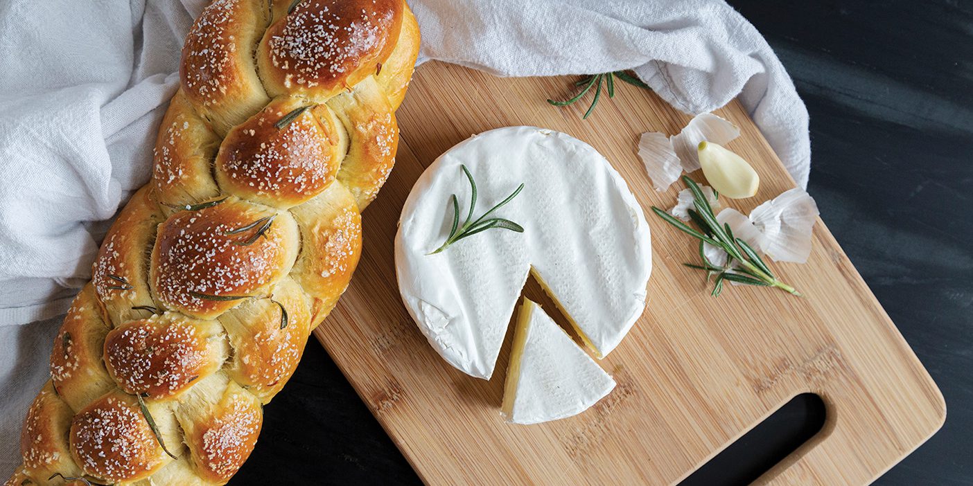 Braided challah bread and brie cheese on top of a wooden cutting board.