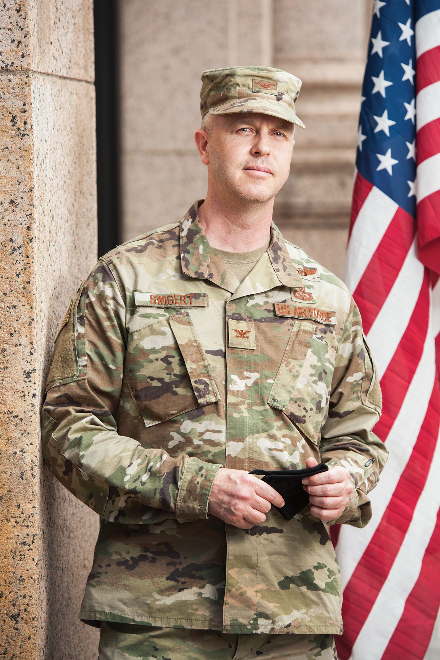 Air Force colonel Brett Swigert in army fatigues standing in front an American flag.