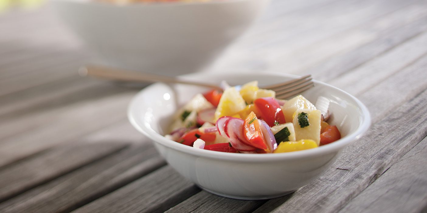 White bowl on a wood table, colorful mango salad inside with a fork.