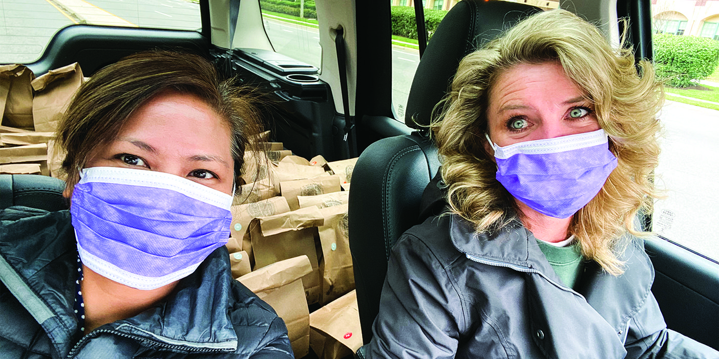 Denise Lee and Lauren Gardner wearing facemasks pose in a delivery van filled with sack lunches.