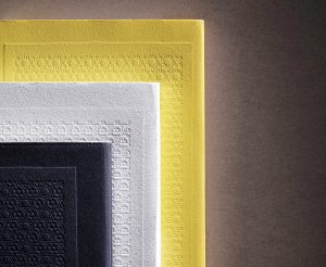 Three books are stacked on top of each other; a small black book, a medium-sized white book, and a large yellow book. The covers are embossed with intricate designs.