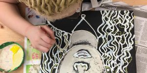 One of Kristen Applebee’s blind students paints a self-portrait on wood using tactile caulk lines.
