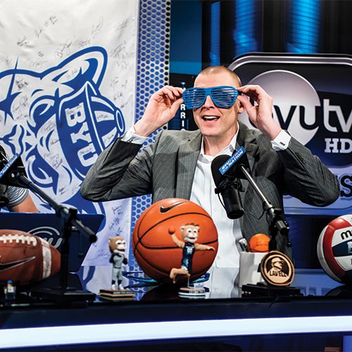 Mark Pope putting on blue glasses at BYUtv's Cougar Nation.