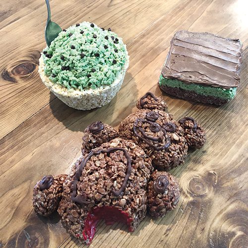 Three treats molded from rice crispy treats sit on a table: a large chocolate cinnamon bear, a BYU mint brownie, and a cup of ice cream.