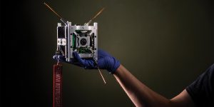 A CubeSat—a small satellite that looks like a metal cube—being held by a hand.