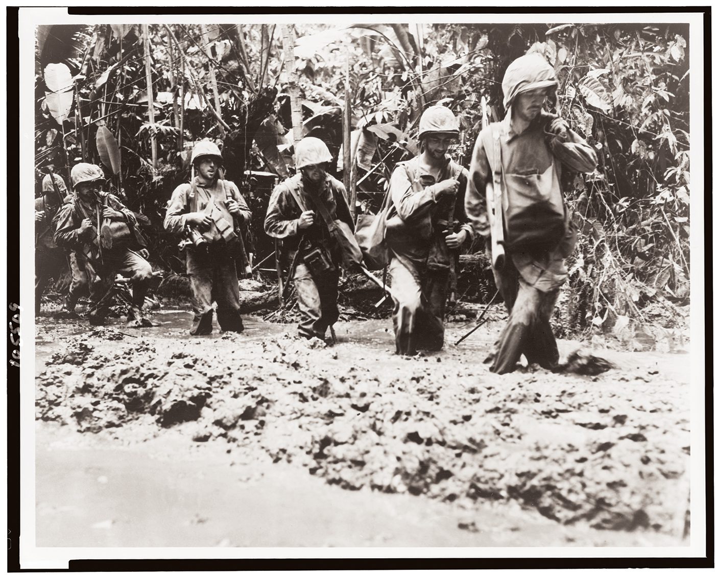 A sepia photo from 1943 shows US marines marching through mud on Bougainville Island, Solomon Islands.