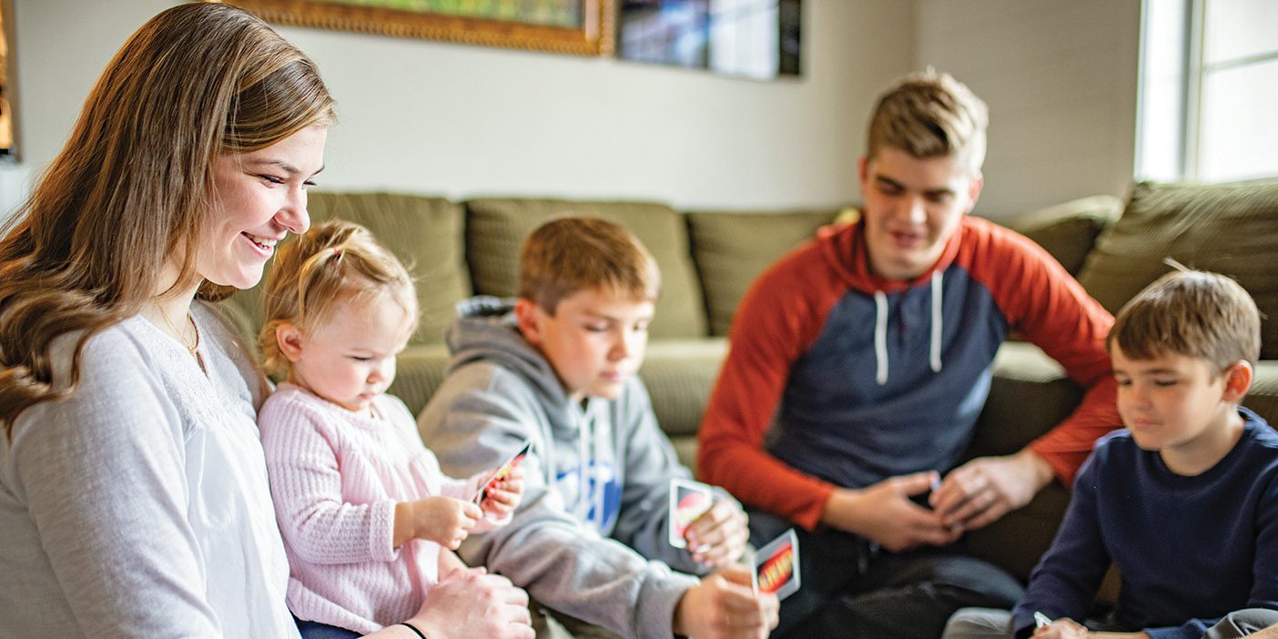 Smiling mother and four children play a game of Uno on the living room floor.