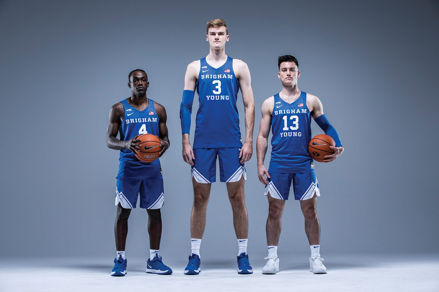BYU men's basketball starters Brandon Averette, Matt Haarms, and Alex Barcello stand in front of a gray backdrop.