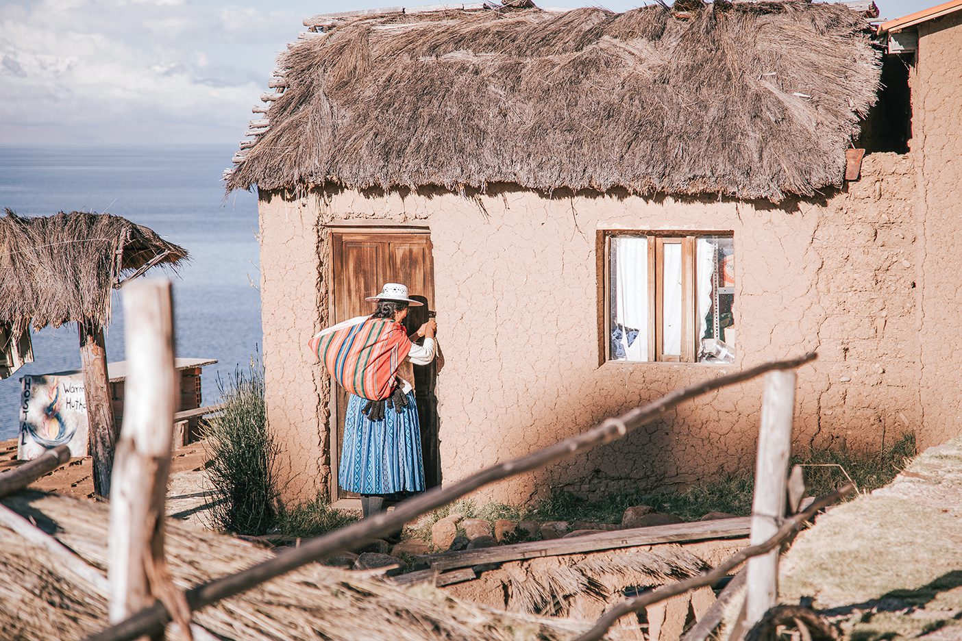 A woman carrying a colorful sack over her shoulder knocks on a traditional Bolivian home.